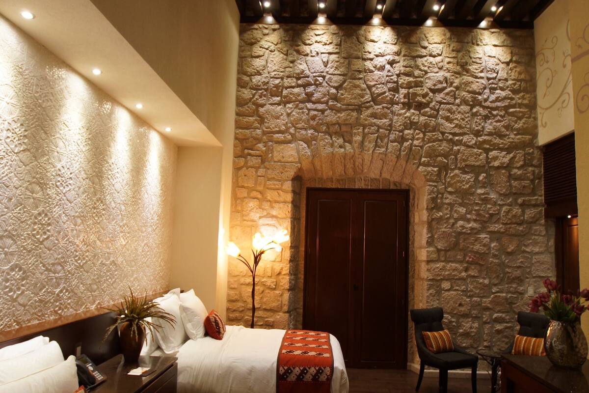 A hotel room with a stone wall, two beds with red and white bedding, a wooden ceiling, and a stone archway.