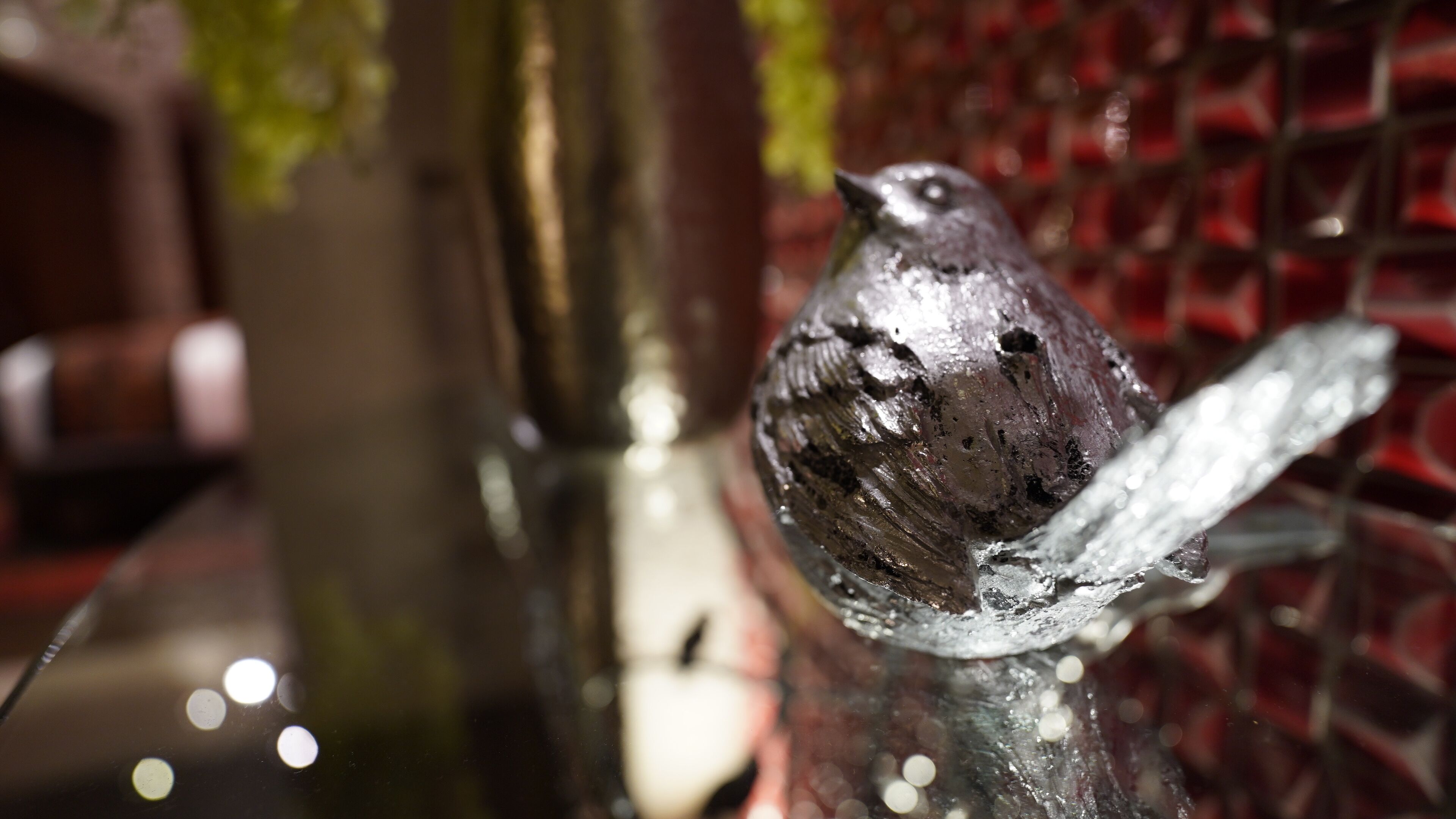 A metallic bird sculpture on a reflective surface.