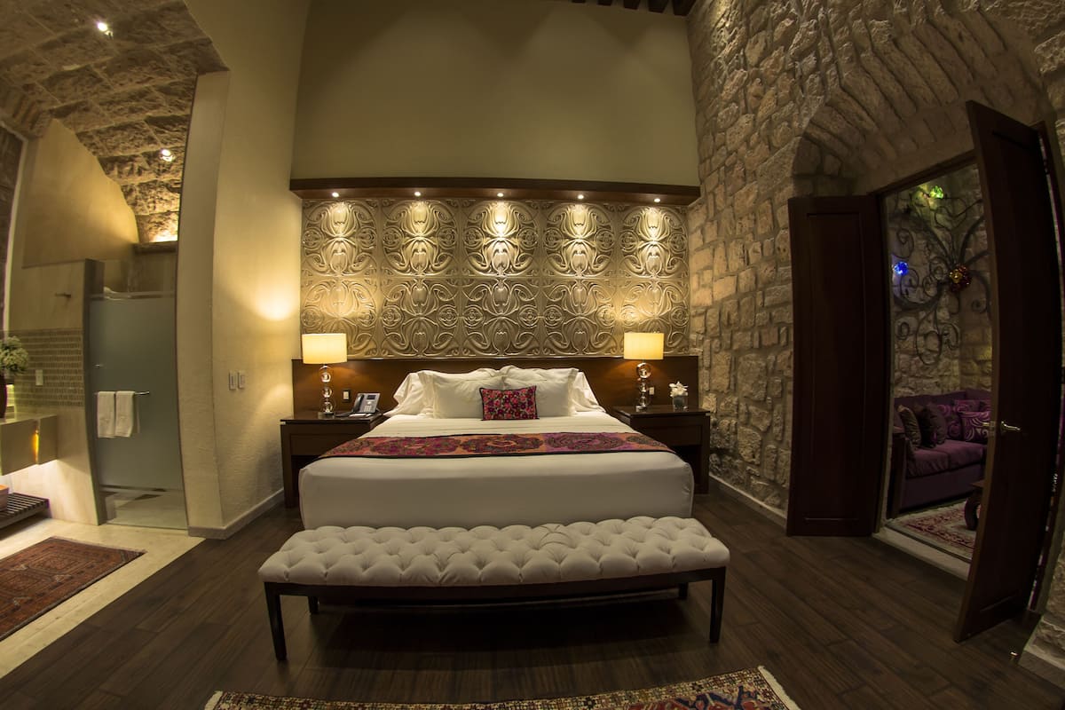 A spacious bedroom with a large bed, a stone accent wall, and a view of a purple sofa through an open door.