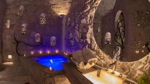 Un área de spa con una pared de piedra, una piscina iluminada en azul y un banco de madera.