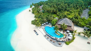 Un resort con una amplia piscina, playa y exuberante vegetación tropical.