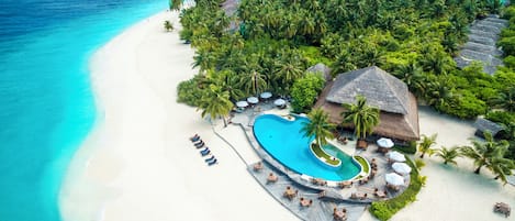 Un complex turístic amb una gran piscina, platja i vegetació tropical abundant.