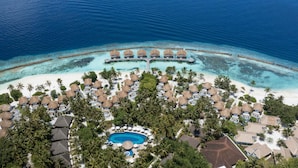 Vista aérea de un complejo turístico con bungalows sobre el agua, una piscina central y una playa.
