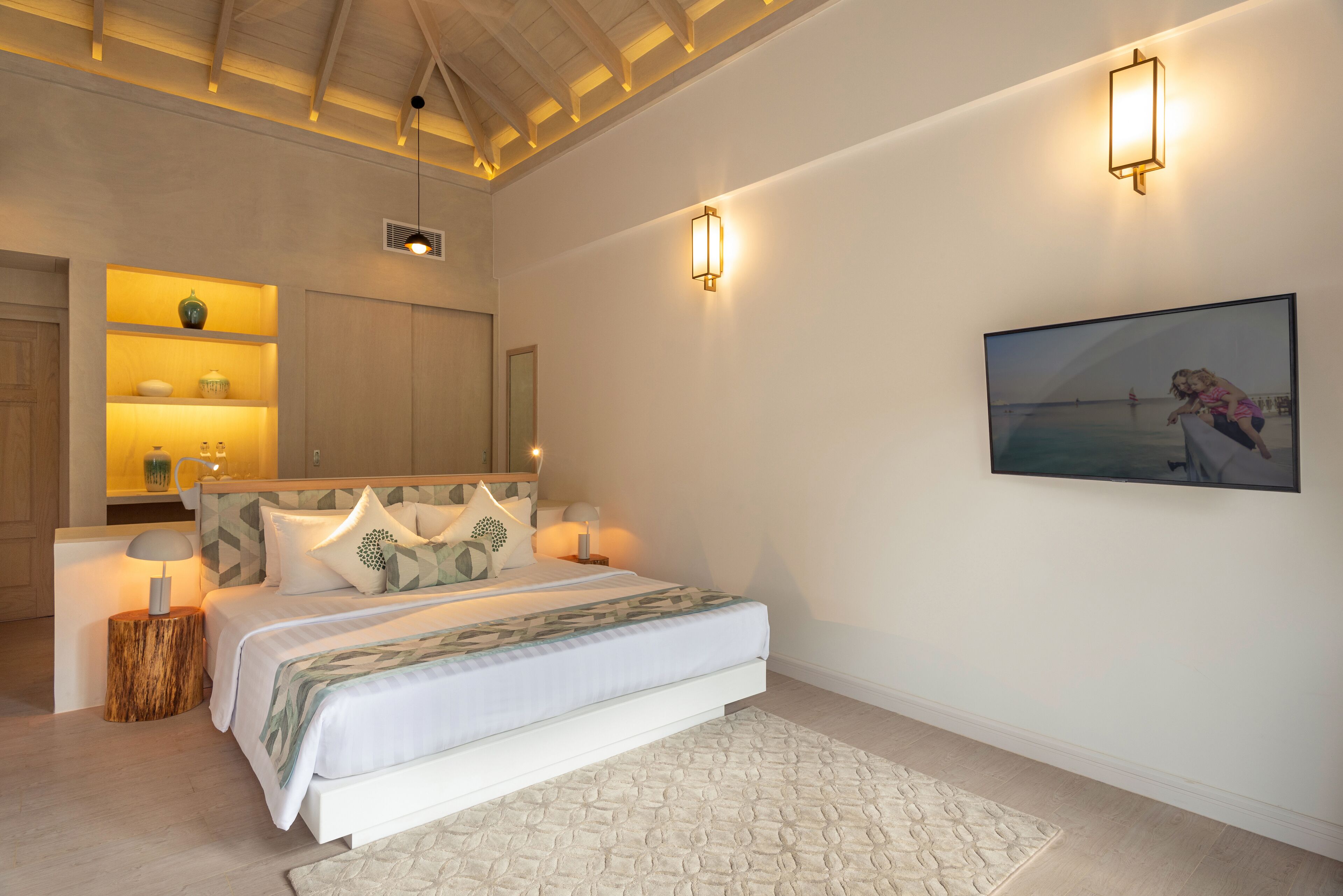 A bedroom with a bed, bedside tables, a nightstand, a wall-mounted TV, and a painting.