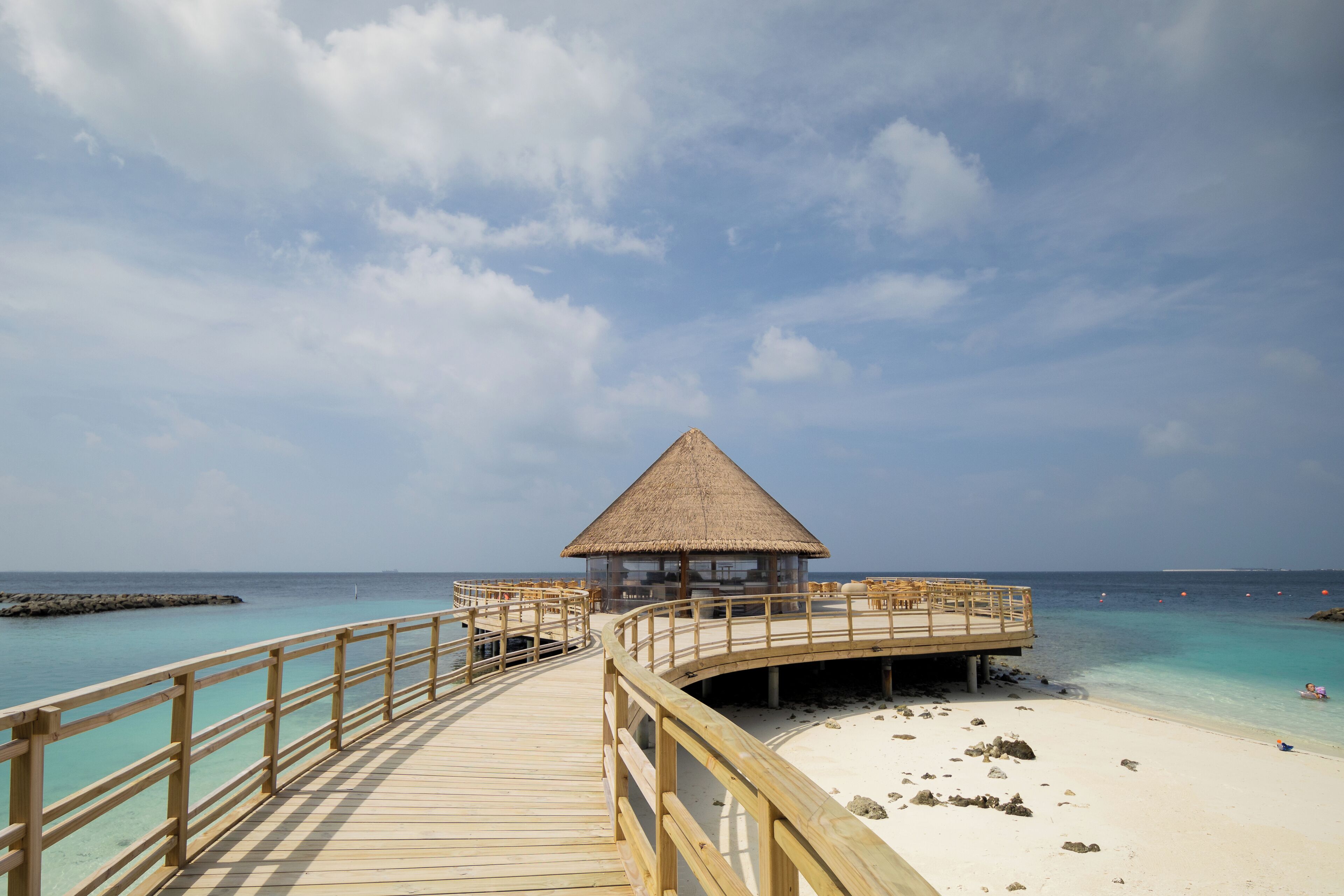 A wooden deck leading to a thatched-roof structure with a view of the ocean.