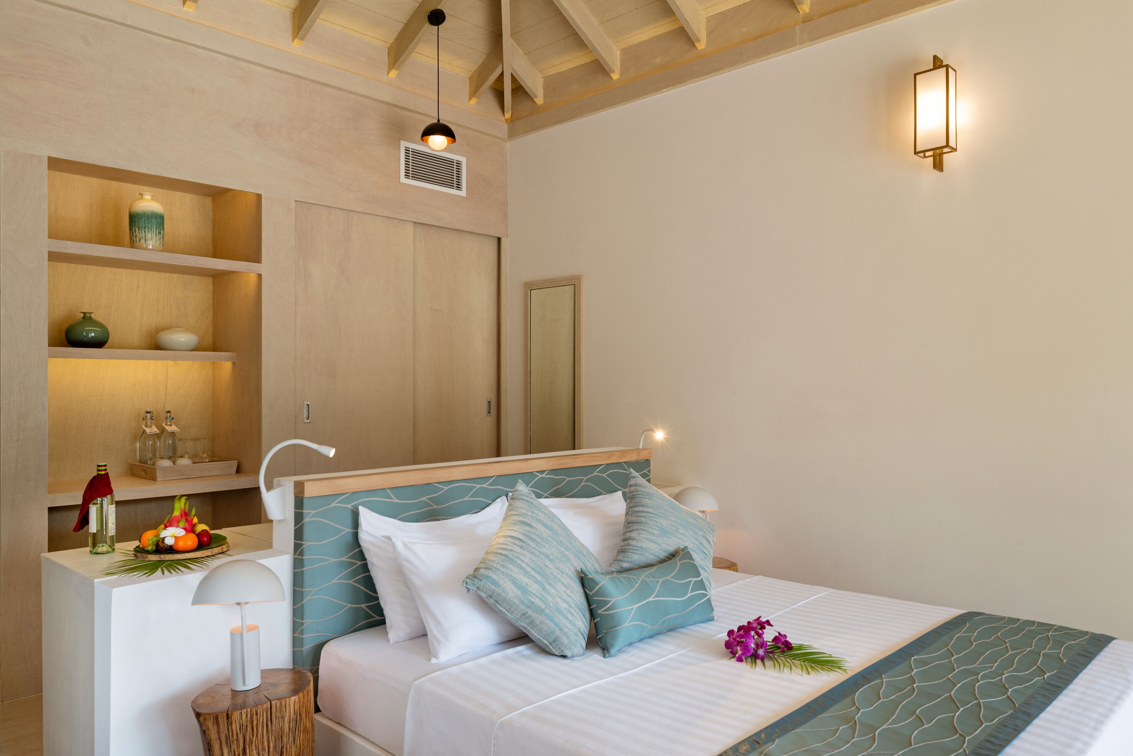 A neatly arranged bedroom with a bed, bedside table, lamp, and shelves with decorative items.