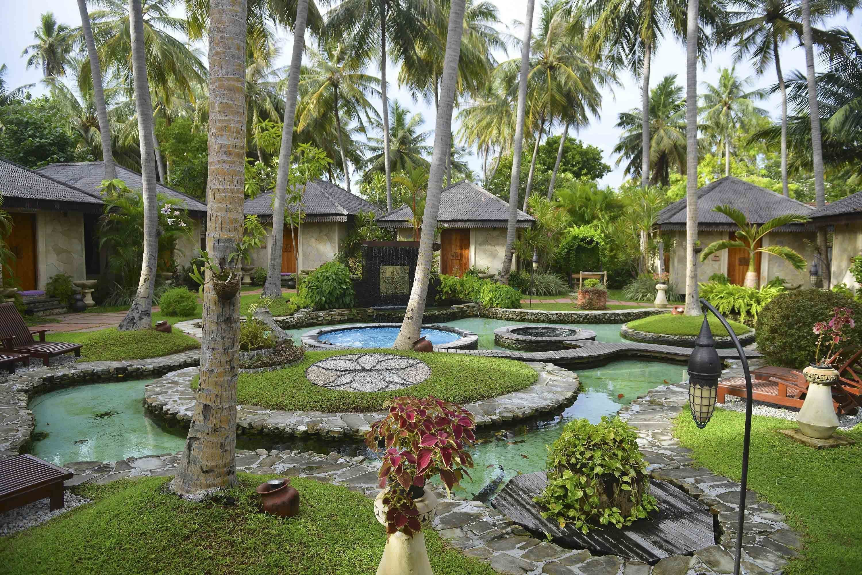 Un resort tropical con varias cabañas sobre el agua, una fuente central y abundante vegetación.