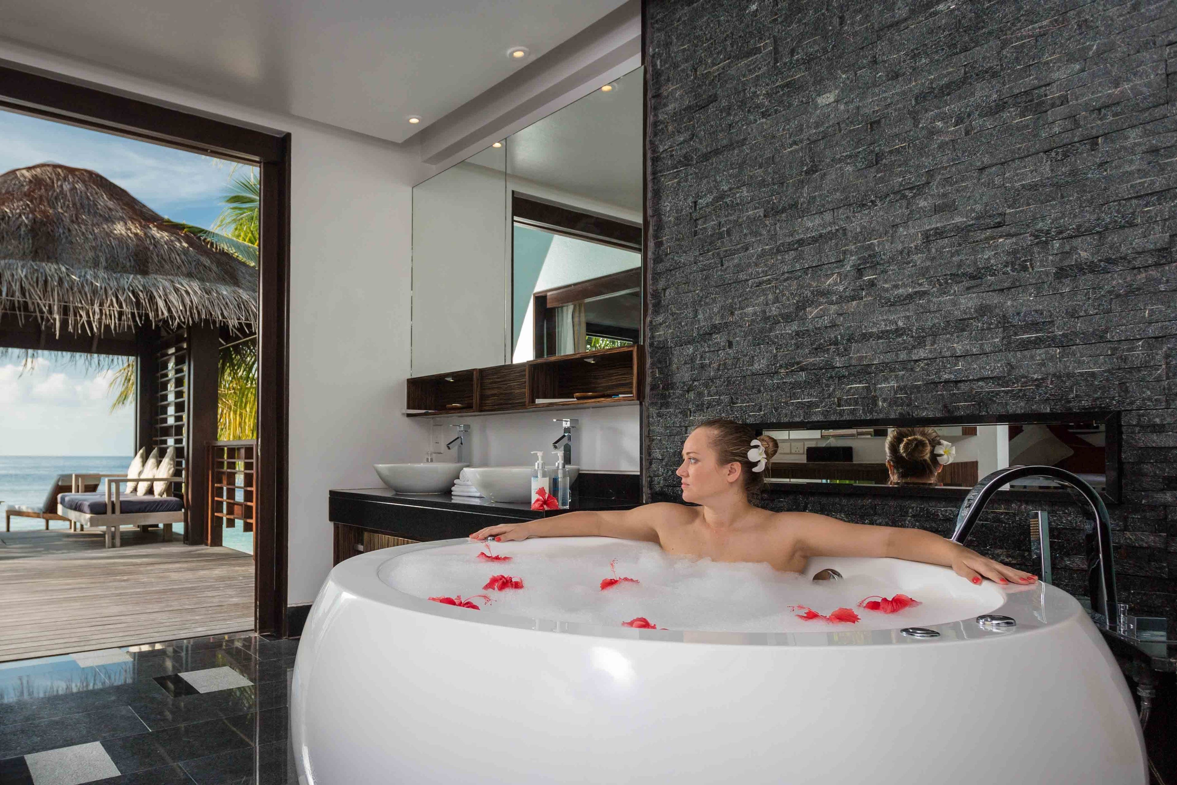 A modern bathroom with a large bathtub, a wooden deck, and a view of the ocean.