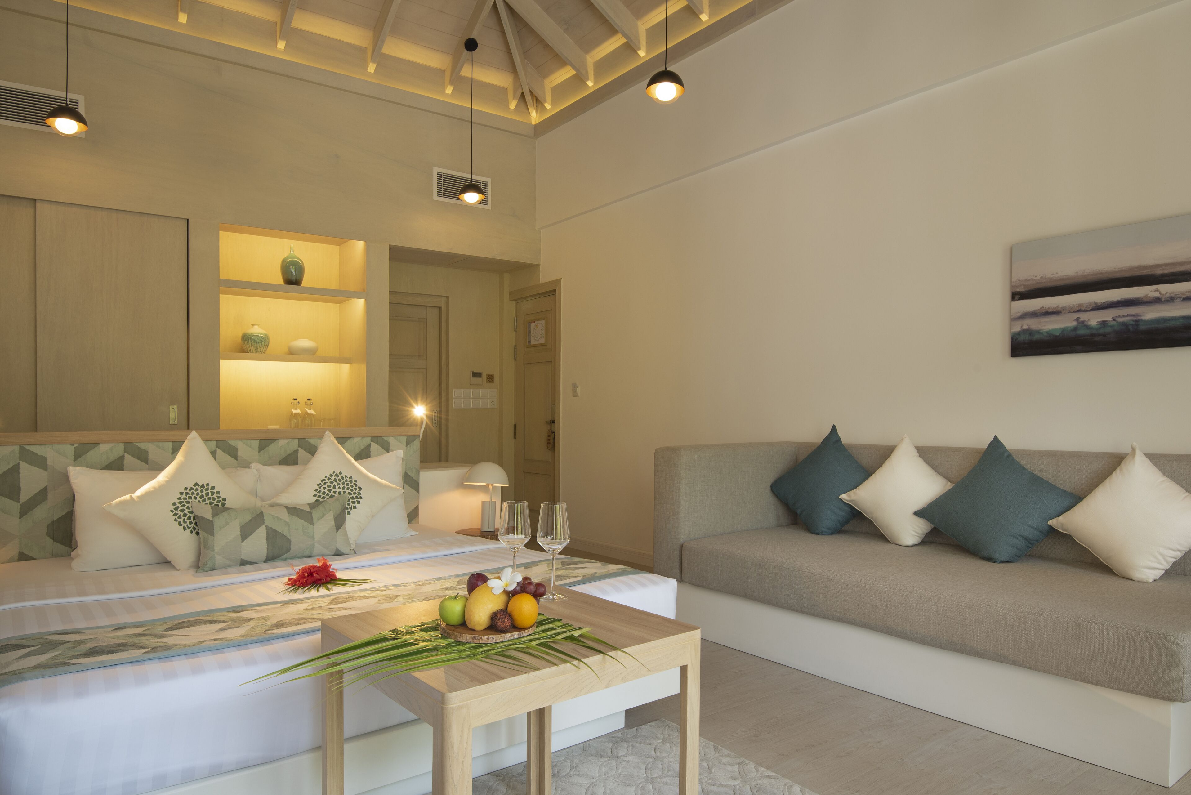 Une chambre d’hôtel moderne avec un lit, un canapé, une petite table avec des fruits et un tableau au mur.