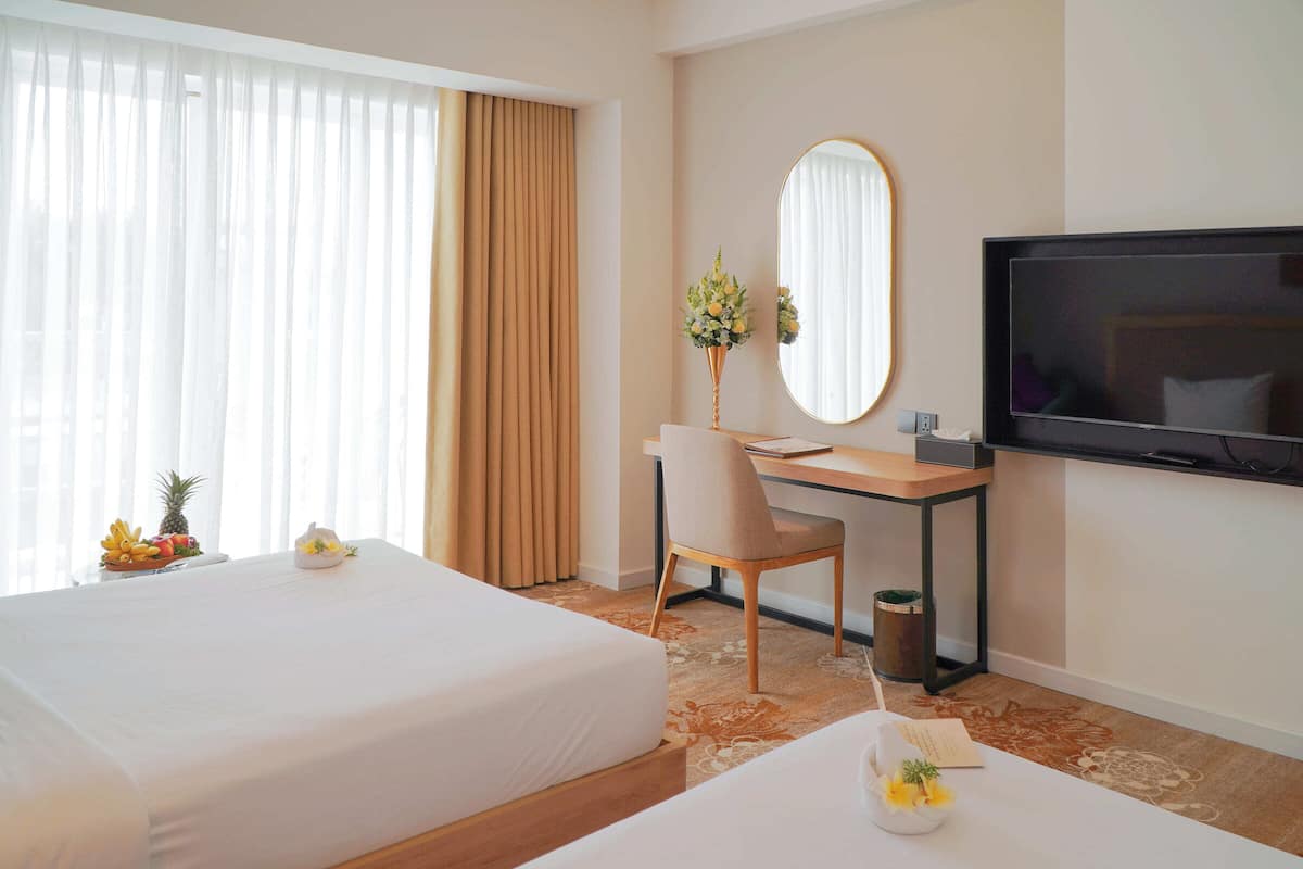 Ett hotellrum med två sängar, ett skrivbord, en tv och ett stort fönster med gardiner.