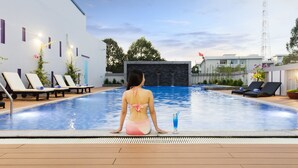 Una mujer sentada junto a una piscina con sillas de descanso y una cascada al fondo.