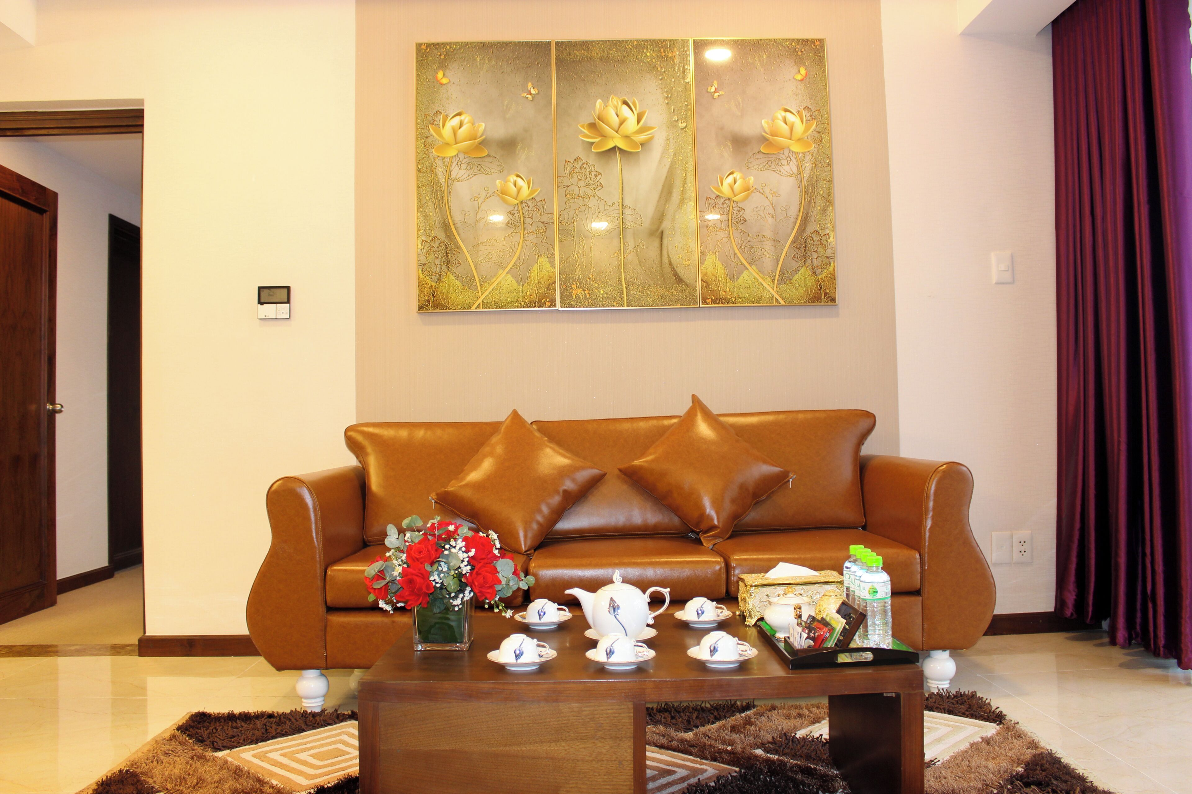 A living room with a brown leather sofa, a coffee table with teacups and a vase of flowers, and a wall art piece above.