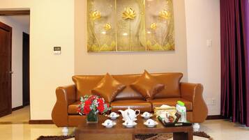 A living room with a brown leather sofa, a coffee table with teacups and a vase of flowers, and a wall art piece above.