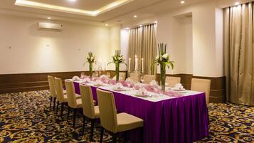 A conference room with a long table set for a meeting, surrounded by chairs, with a patterned carpet and curtains.