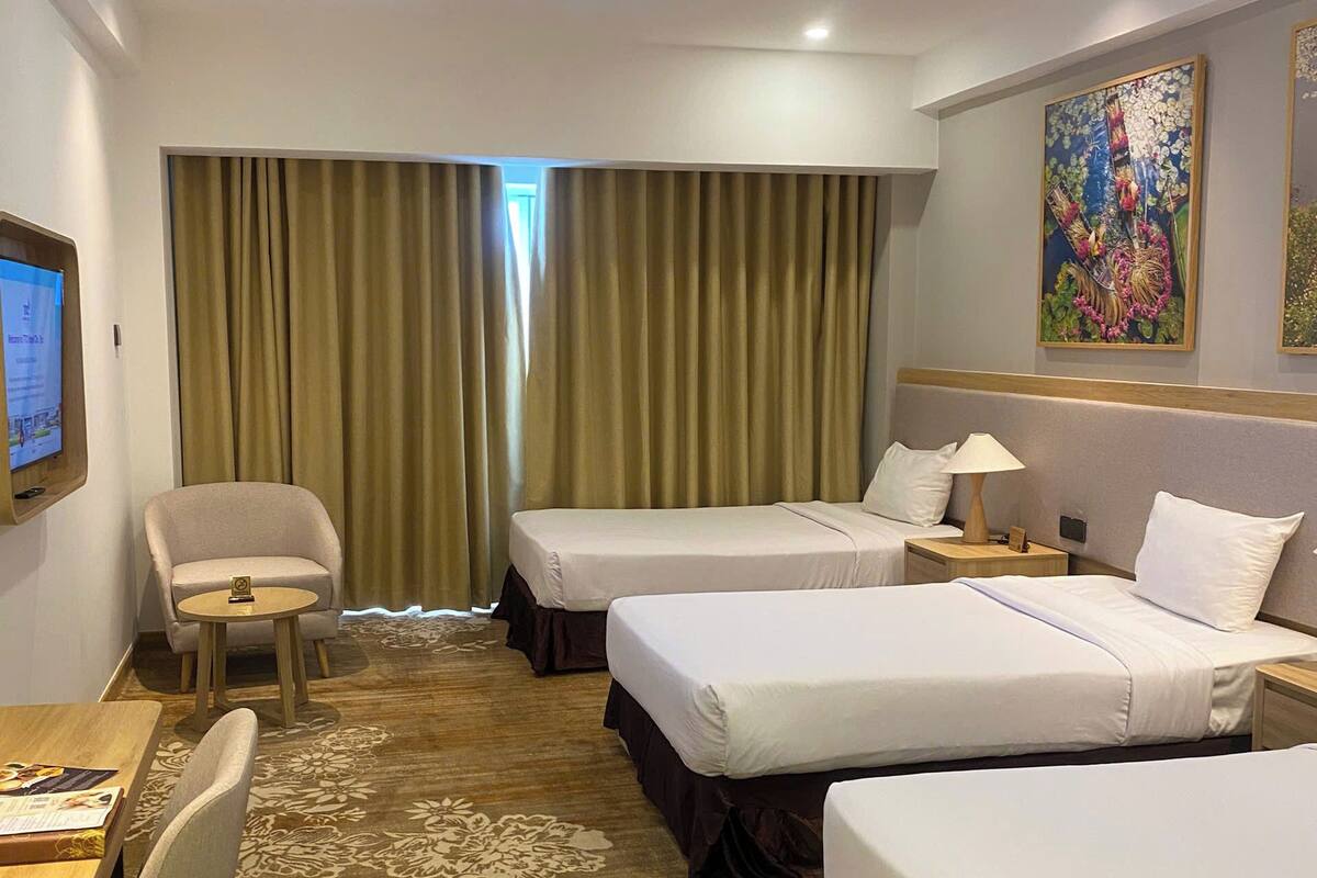 Ett hotellrum med två sängar, ett skrivbord, en stol, en tv och en tavla på väggen.