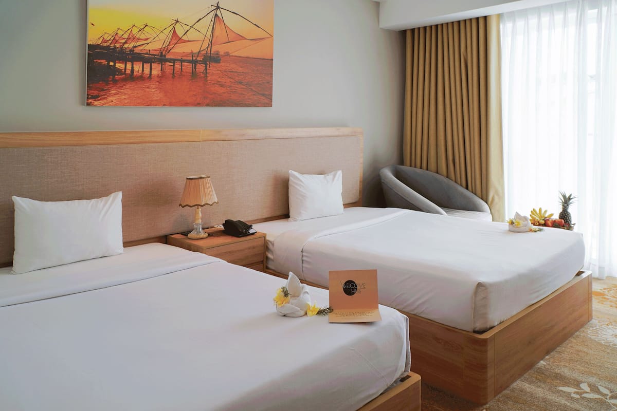 Ett hotellrum med två sängar, ett nattduksbord med en lampa, en tavla på väggen och en fruktskål på nattduksbordet.