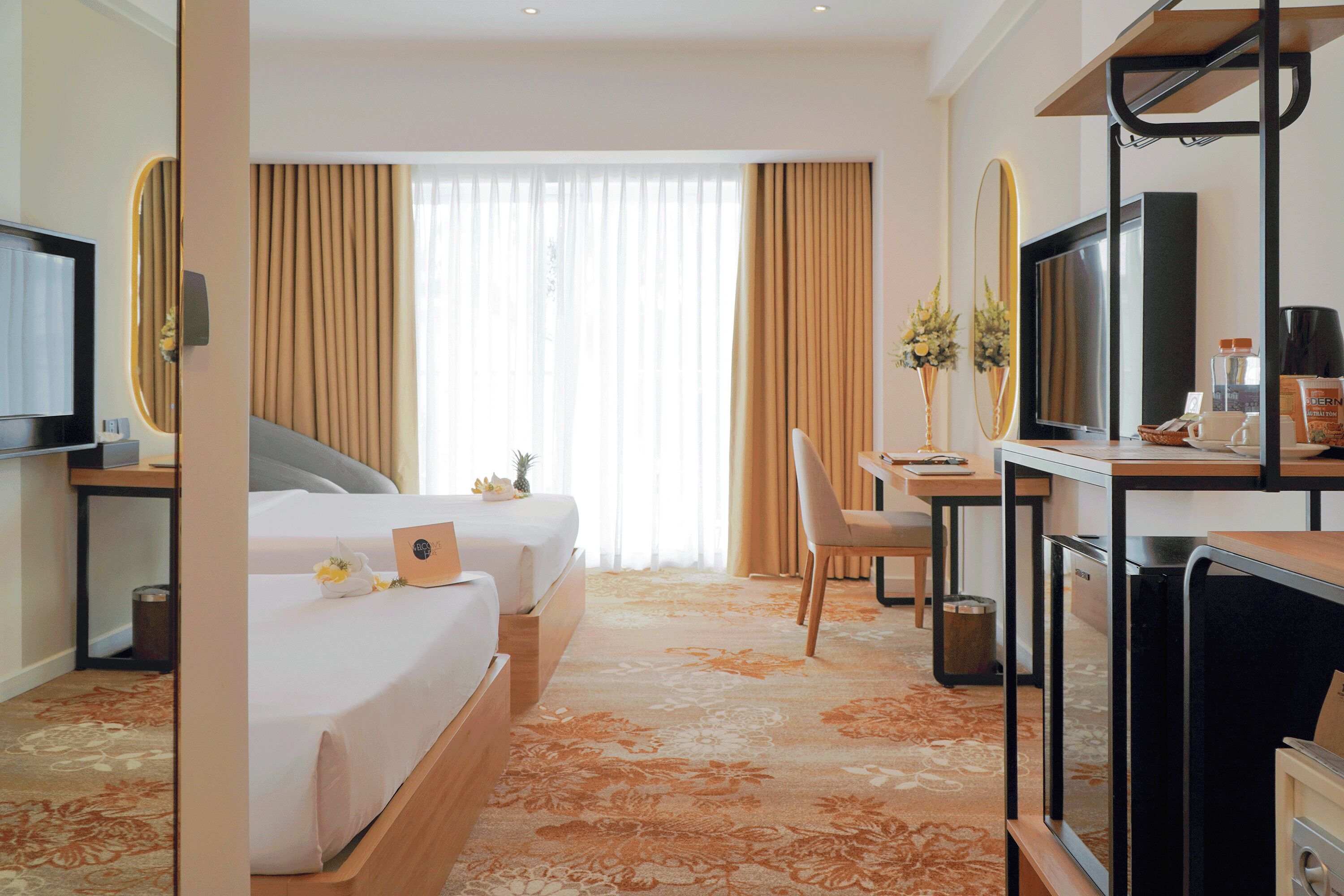 A hotel room with two beds, a desk, a television, and a large window with curtains.