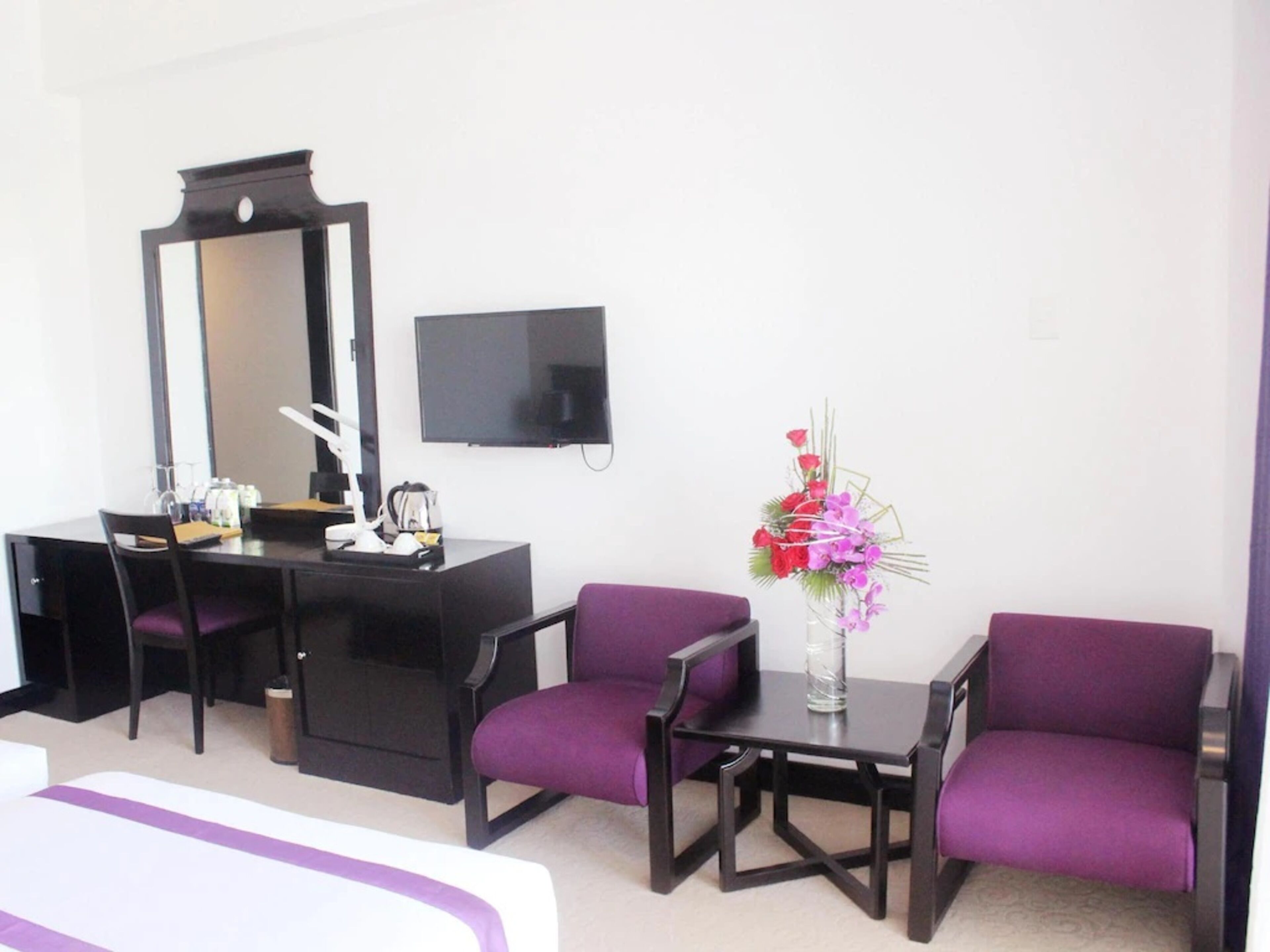 Habitació d'hotel amb un llit, escriptori amb cadira, prestatge, televisió de pantalla plana i un vas amb flors.