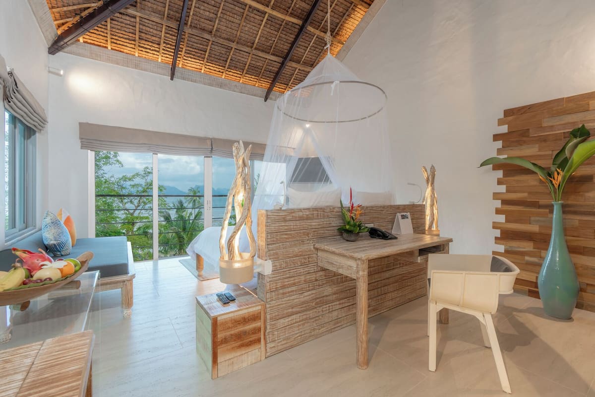Een moderne kamer met een houten bureau, een bank en een eethoek. Grote ramen bieden uitzicht op het omliggende landschap.
