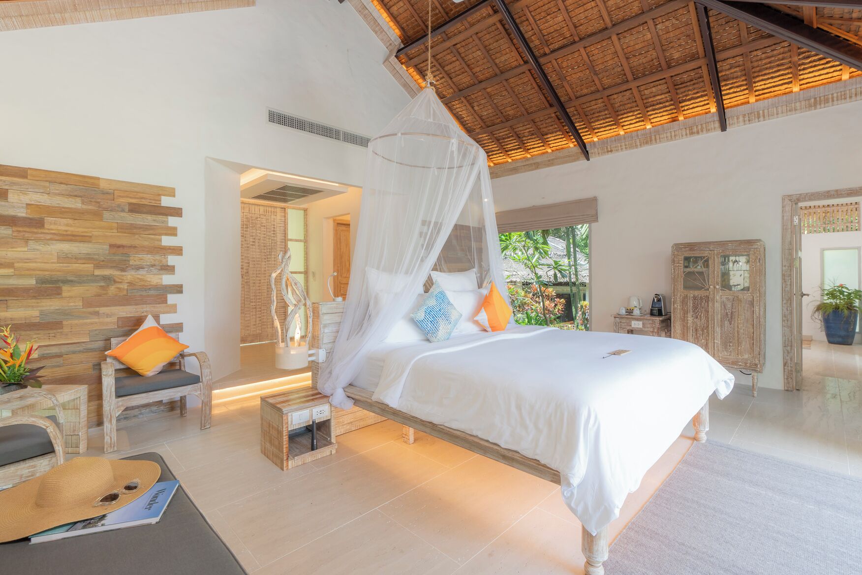 A spacious bedroom with a large bed, a wooden headboard, a nightstand, a chair, and a potted plant.