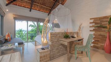 A spacious room with a bed, a wooden desk, a chair, and a large window offering a view of palm trees.