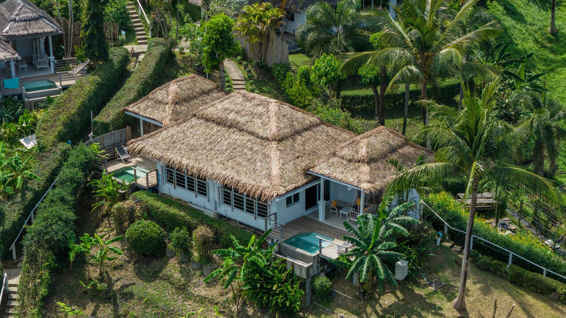Ein Haus mit Strohdach und Pool, umgeben von üppiger Vegetation und Palmen.