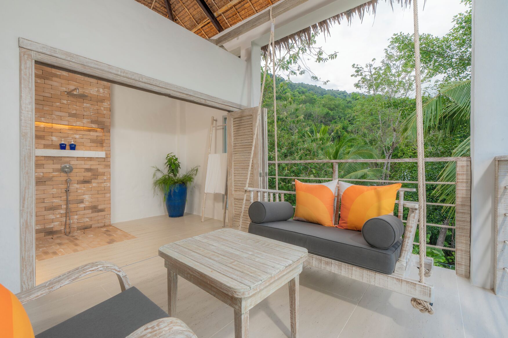 A room with a swing seat overlooking a lush green landscape, a brick shower, and a white table.