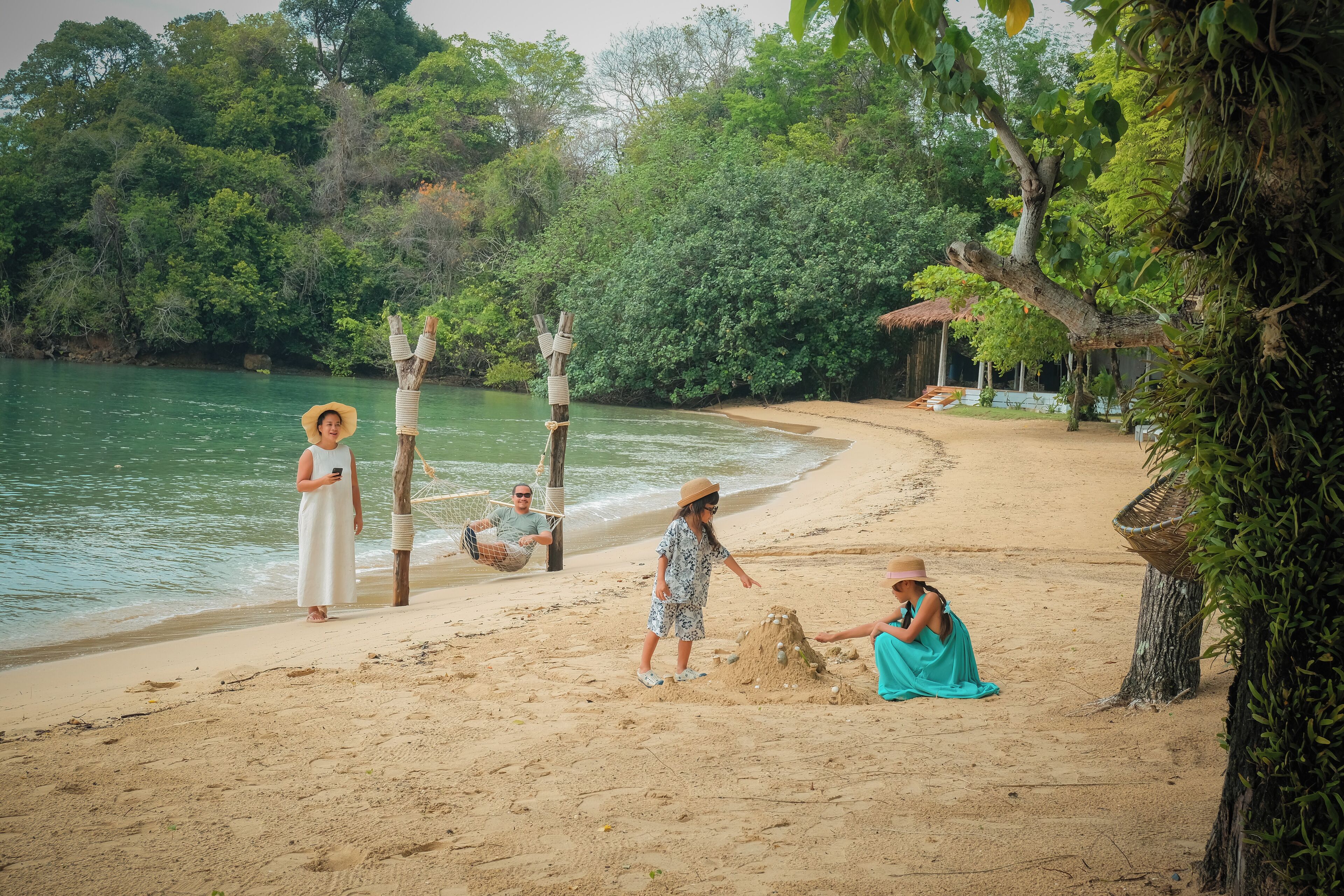 Une plage de sable avec un hamac, une personne vêtue d’une robe blanche et une autre vêtue d’une robe bleue.
