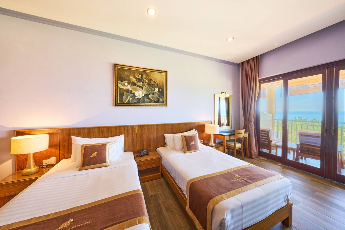 A hotel room with two beds, a desk, a chair, a large window with a view, and a painting on the wall.