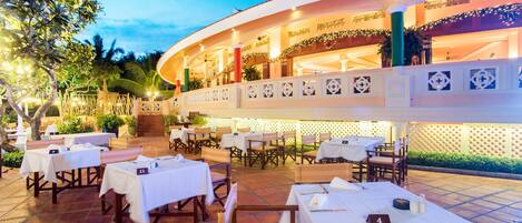 A restaurant with outdoor seating, white tables, and a covered area with a balcony.