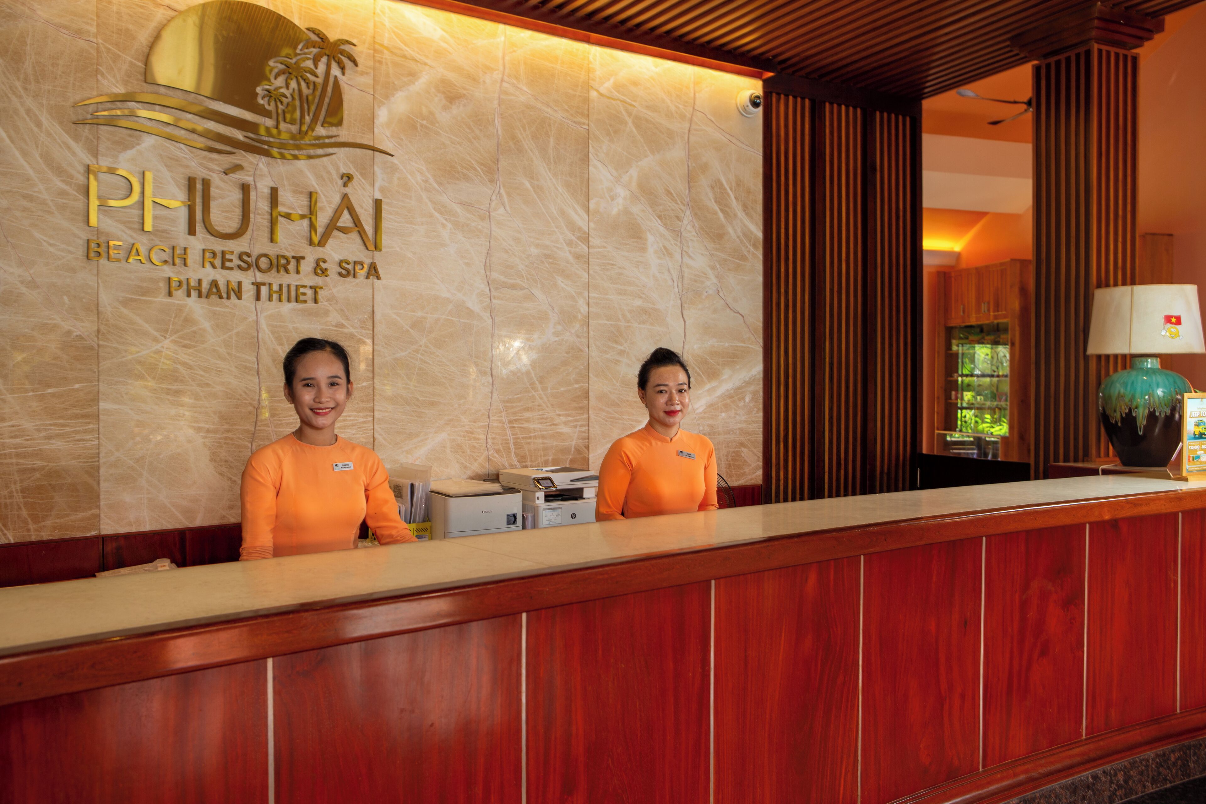 Mostrador de recepción en Phu Hai Beach Resort & Spa con dos empleados, una pared de mármol y paneles de madera.
