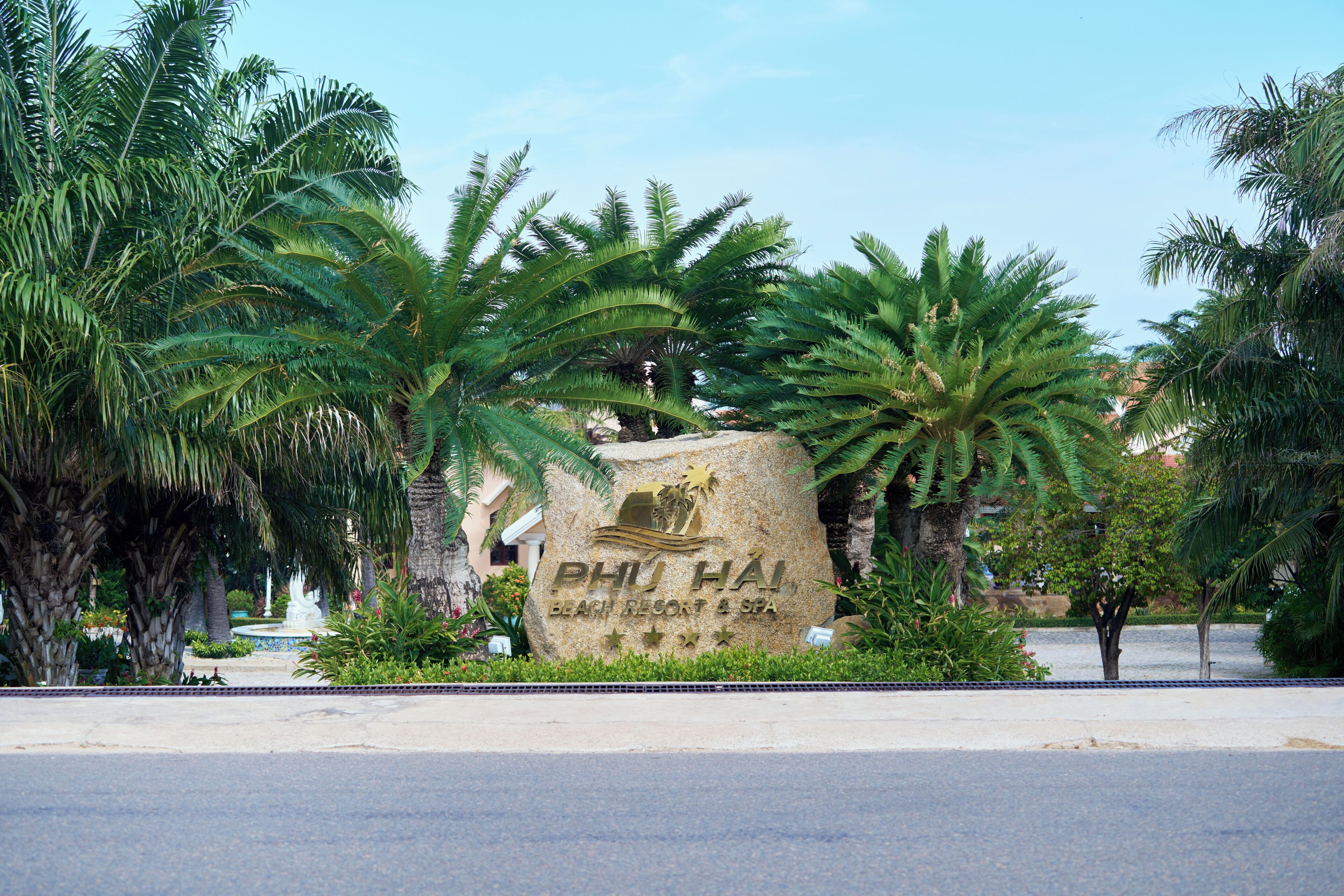 En stor sten med teksten "PHU HAI" og "BEACH RESORT & SPA" indgraveret, omgivet af frodig vegetation.