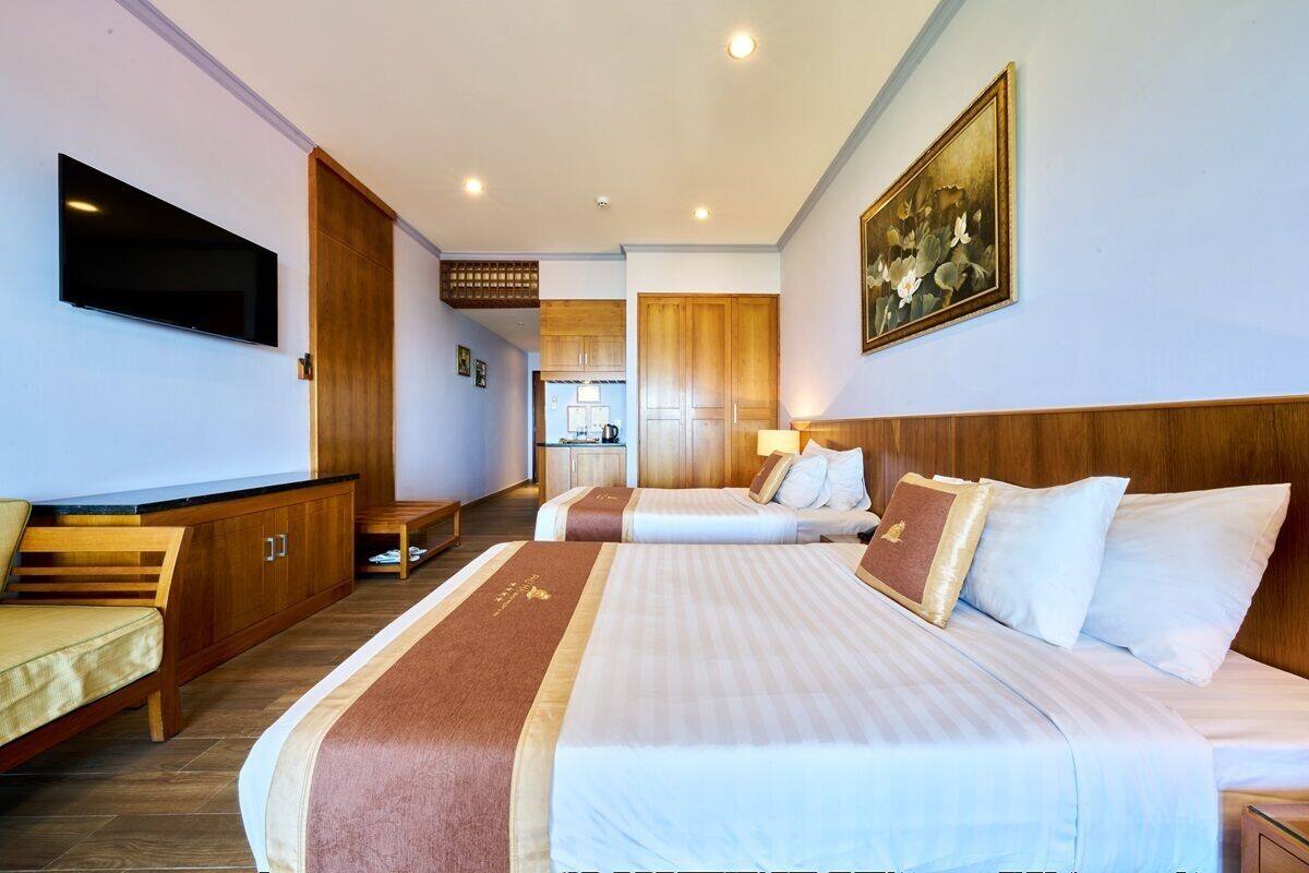 A hotel room with two beds, a TV, a painting, and a kitchenette in the background.