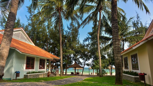 A resort with palm trees, a beach view, and a thatched-roof gazebo.