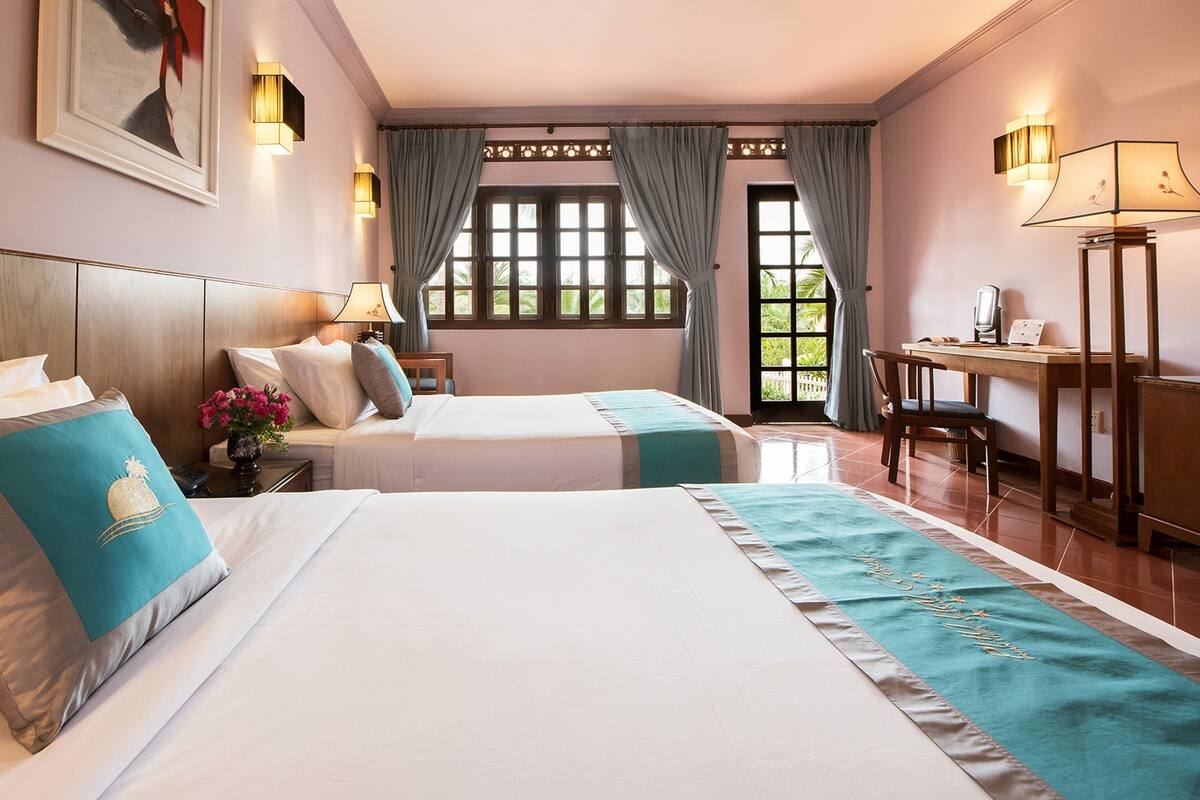 A hotel room with two beds, a desk, a chair, and a window with curtains.