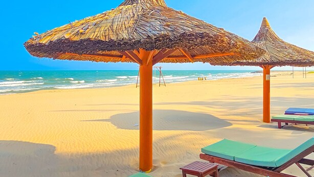 Una playa con sombrillas de paja y sillones de madera.