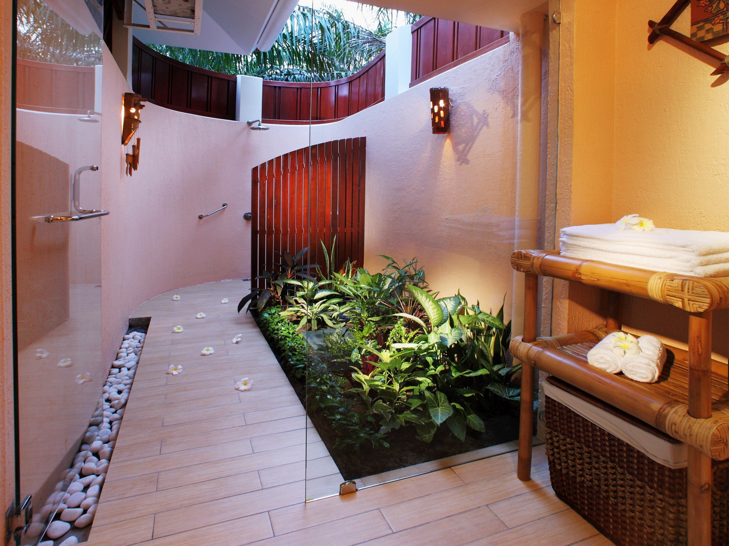 A spa area with a wooden floor, a small garden with plants, a bamboo shelf with towels, and a shower area.