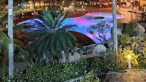 Vista nocturna de un complejo turístico con piscina, palmeras y zonas de estar al aire libre.