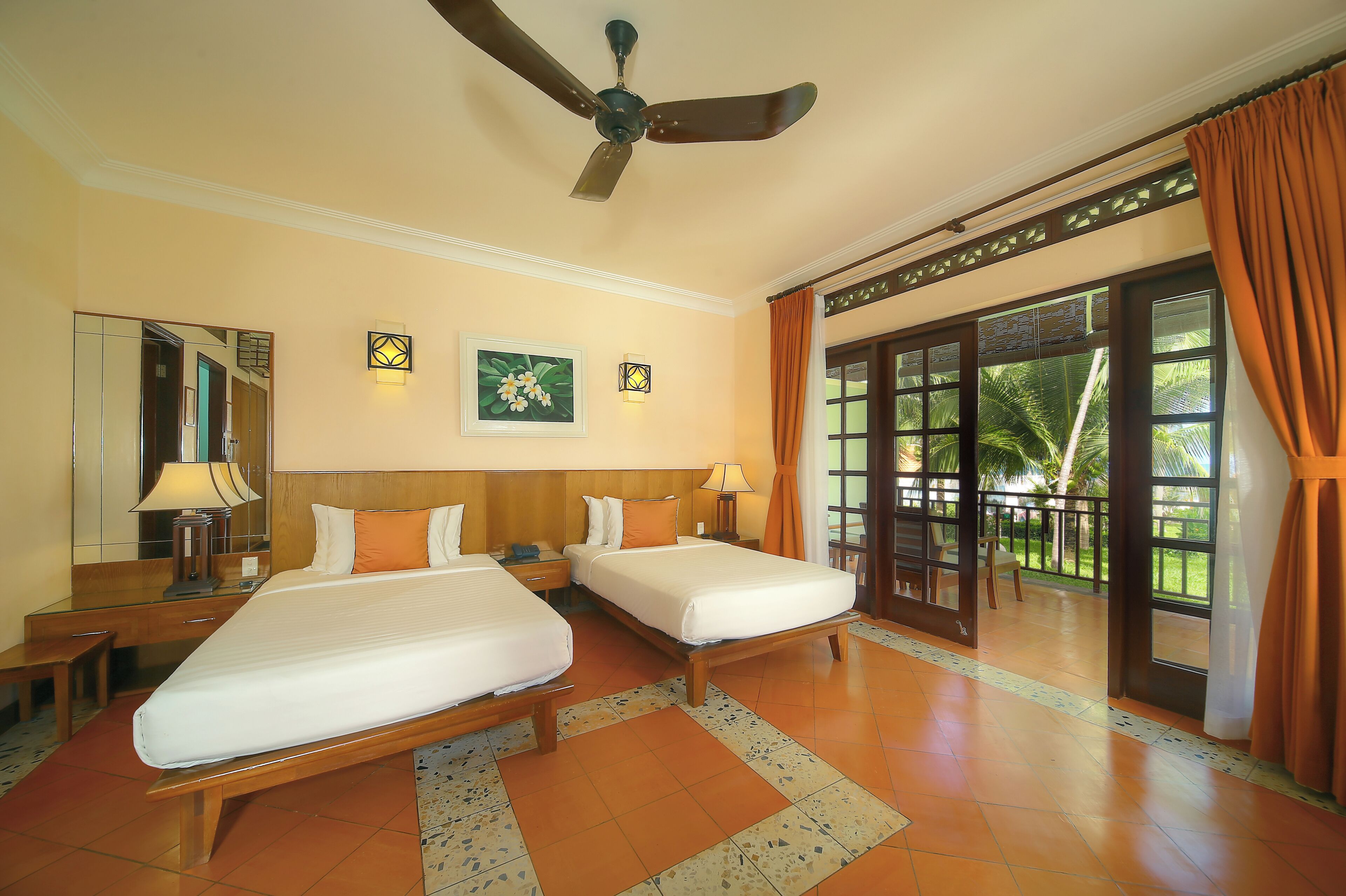 A hotel room with two beds, a ceiling fan, a large window with curtains, and a view of palm trees.