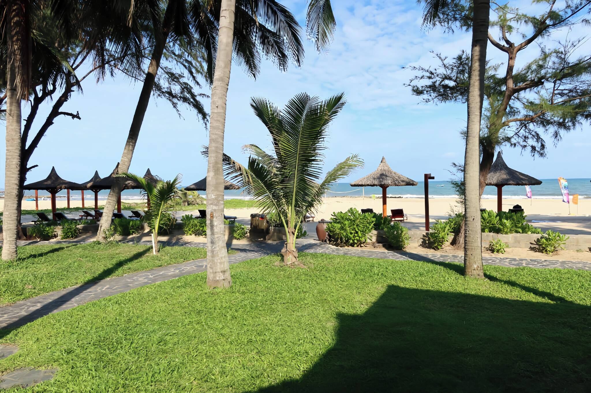 Un jardín tropical con palmeras, un sendero y sombrillas de playa.