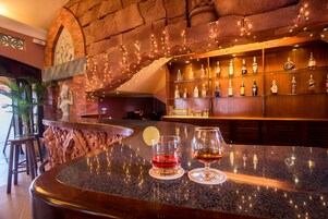 Zona de bar con una encimera de granito curvada, dos vasos de bebidas rojas y ámbar, y una variedad de botellas en estanterías.