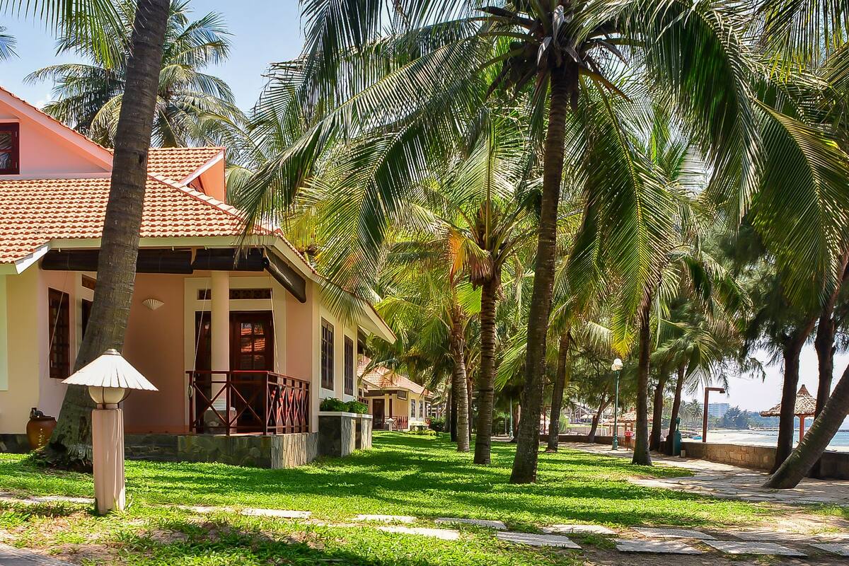 A beachfront property with a row of palm trees, a tiled roof, and a beachside view.