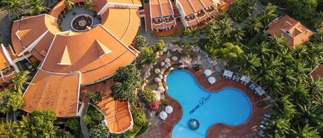 An aerial view of a resort with a swimming pool, palm trees, and resort buildings.