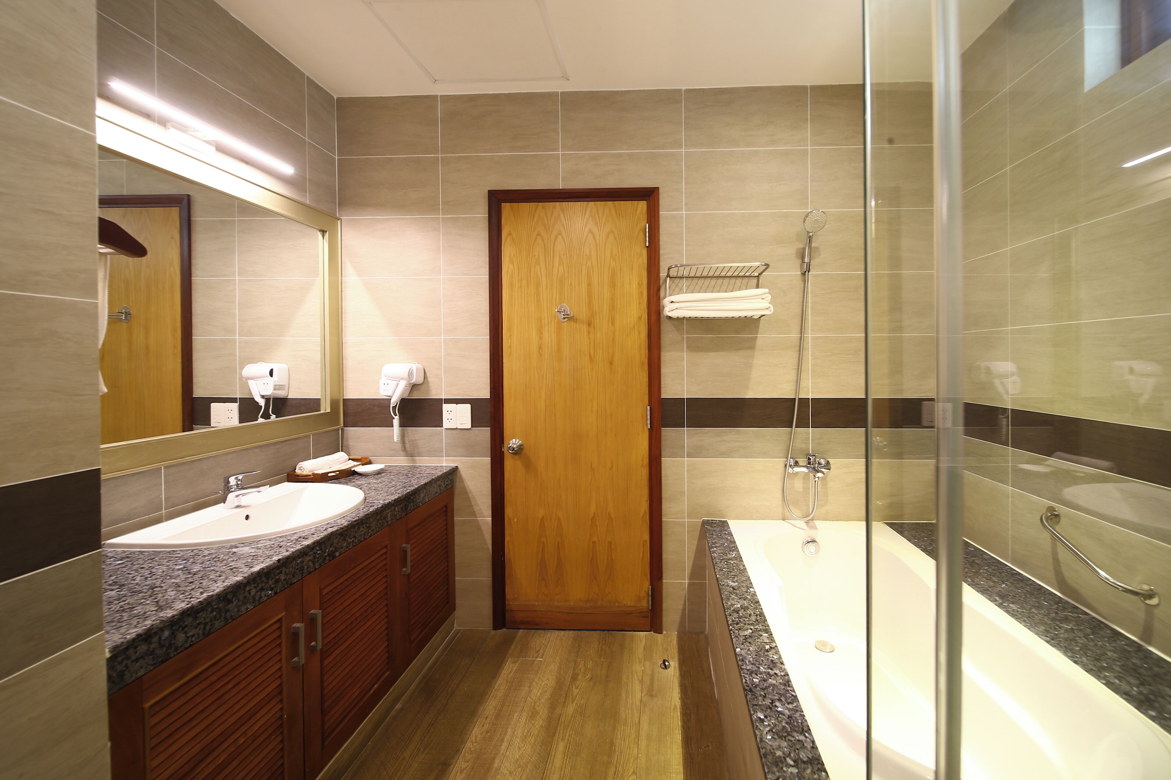 Un bany modern amb una porta de fusta, un lavabo, una banyera i una zona de dutxa amb envàs de vidre.