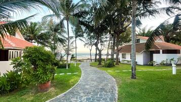 A pathway leading to a beach with palm trees and a building with a red roof.
