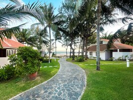A pathway leading to a beach with palm trees and a building with a red roof.