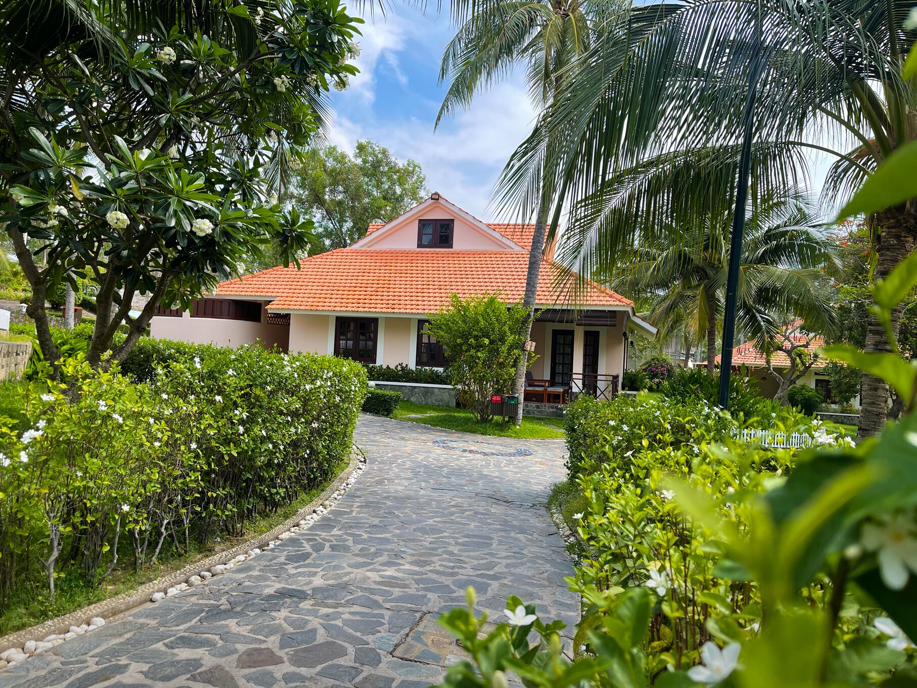 A house with a tiled roof, surrounded by lush greenery and a stone pathway leading to the entrance.