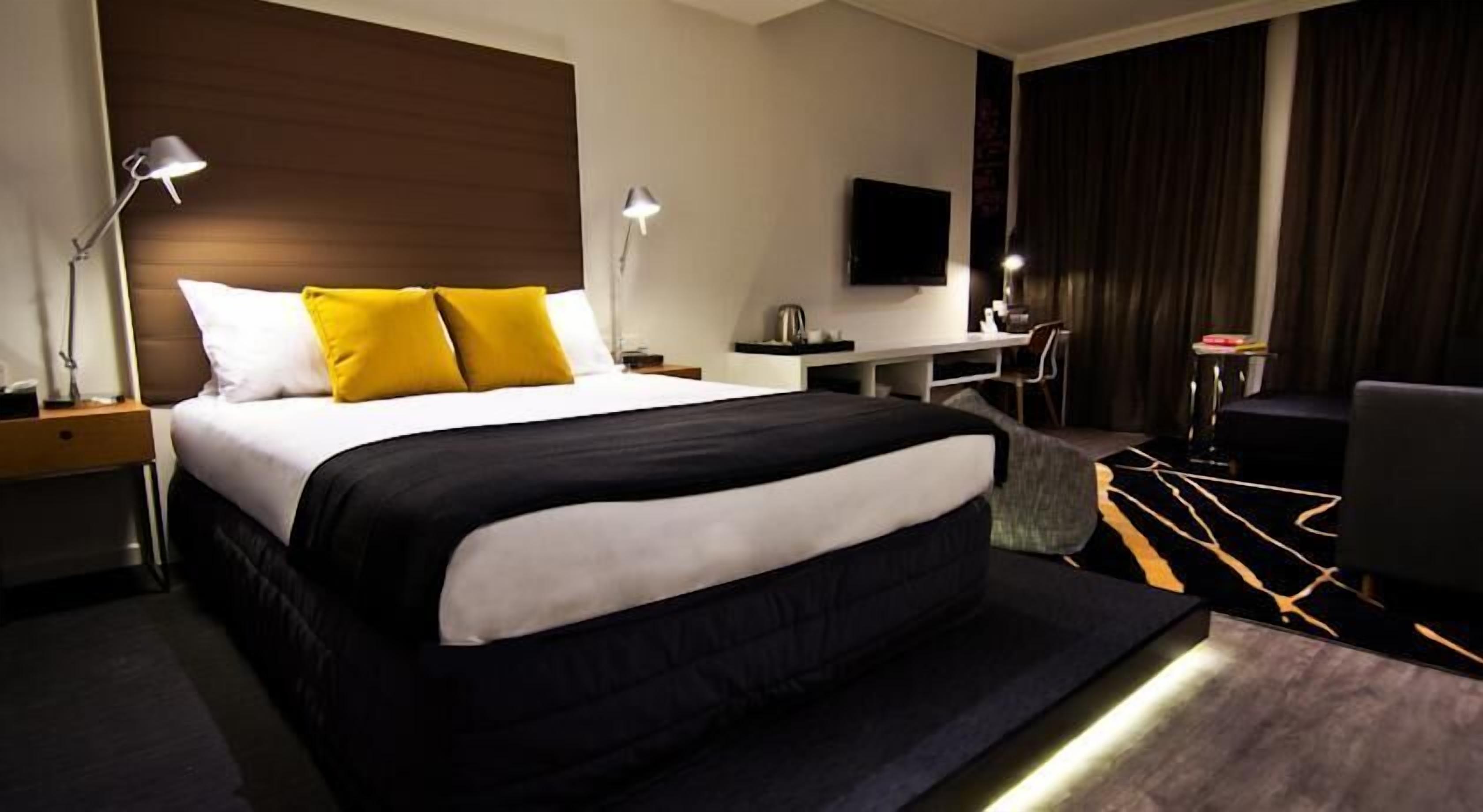 Ett modernt hotellrum med en stor säng, sänglampor, ett skrivbord och en platt-TV.