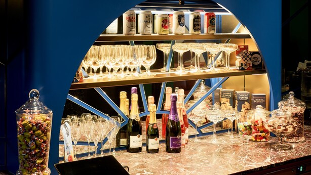 A bar area with a blue backdrop, shelves stocked with bottles, glasses, and a variety of snacks. - Laneways by Ovolo (Melbourne)