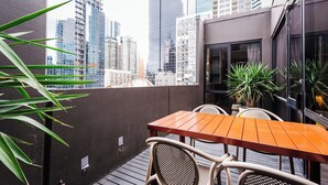 A balcony with a wooden table and chairs, surrounded by tall buildings. - Laneways by Ovolo (Melbourne)